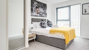 A modern bedroom with a bed, bedside table, and a large window with blinds. - Apollo Luxury - Netflix - Fast WIFI (West Midlands)