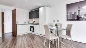 A modern kitchen with white cabinets, a built-in microwave, and a dining area with a glass table and chairs. - Luxe Getaway - Business | Netflix | WiFi (West Midlands)