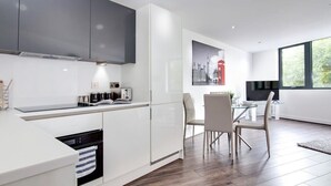 A modern kitchen with white cabinets, a built-in oven, and a dining area with a glass table and chairs. - Luxe Getaway - Business | Netflix | WiFi (West Midlands)