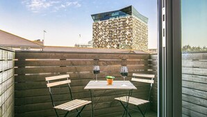 Una terrazza sul tetto con una recinzione in legno, due tavoli con sedie e due bicchieri da vino.