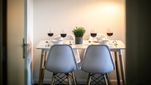 Zona pranzo con tavolo imbandito per due persone, due sedie, una pianta in vaso e bicchieri da vino.