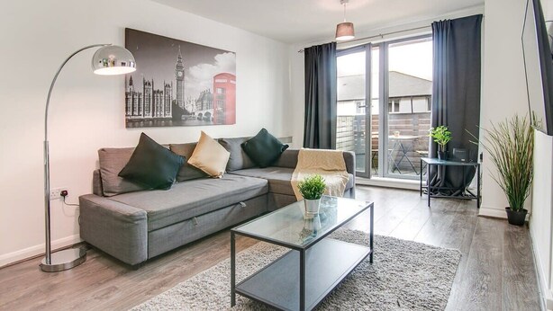 Un soggiorno moderno con un divano angolare grigio, un tavolino in vetro e un quadro raffigurante un panorama urbano.