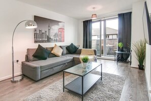 A modern living room with a grey sectional sofa, a glass coffee table, and a cityscape painting on the wall.