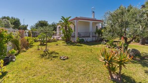A house with a red-tiled roof, a small porch, and a garden with various plants and a lawn. - 2864 Villa Carminella by Barbarhouse (Lecce)
