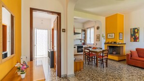 A spacious living area with a dining table, chairs, and a red sofa. A kitchen is visible in the background with a fireplace and various decorations. - 2864 Villa Carminella by Barbarhouse (Lecce)