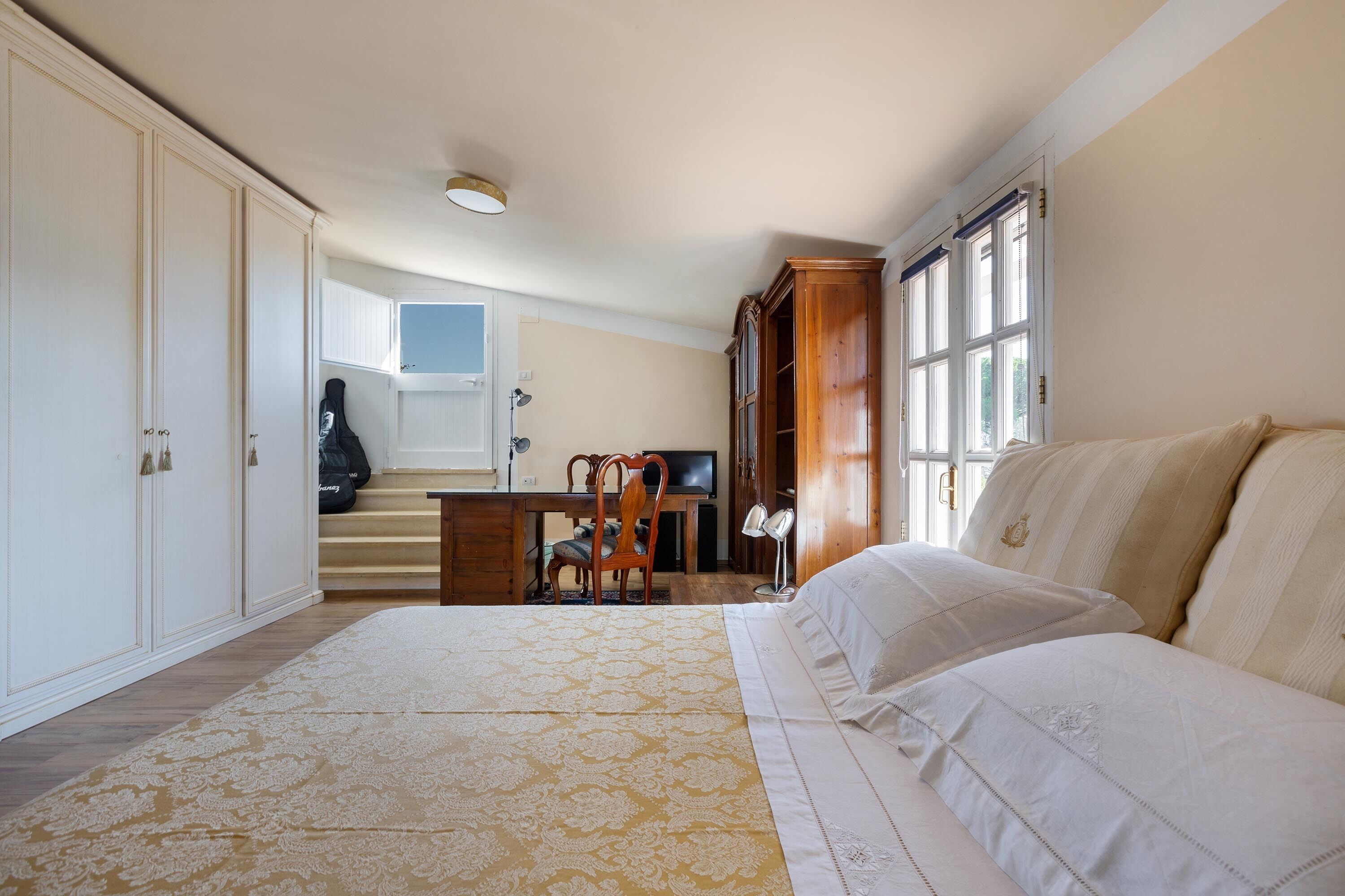Une chambre avec un grand lit, un bureau et une chaise. La chambre est également équipée d’une armoire et d’un téléviseur.