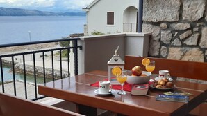A balcony with a table set for breakfast, overlooking a body of water and a mountainous landscape. - Apartments Cumbelic (Mljet)