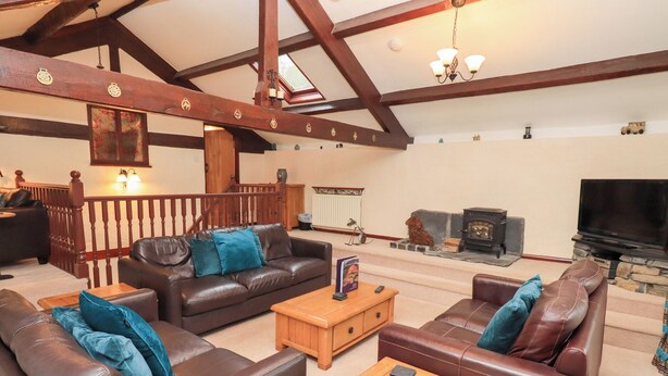 A spacious living room with leather sofas, a wooden coffee table, and a stone fireplace. - Old Coach House (Ambleside)