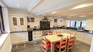 A modern kitchen with white cabinets, a central island with a wooden table and chairs, and a black stove. - Old Coach House (Ambleside)