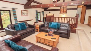 A spacious living room with leather sofas, a wooden coffee table, and a staircase with wooden railings. - Old Coach House (Ambleside)