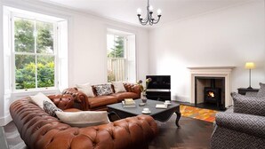 A living room with a brown leather sofa, a black coffee table, a fireplace, and a television. - Ben House (Ambleside)
