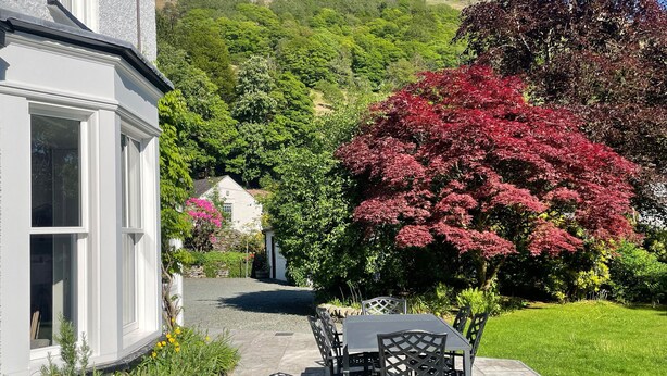 A patio with a table and chairs, a stone pathway, and a house with a white exterior. - Ben House (Ambleside)