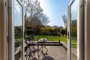 Un patio con piso de piedra, sillas de metal y una mesa con tetera y tazas.