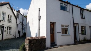 A white building with a stone foundation, a wooden door, and a small window. - Gable End (Keswick)