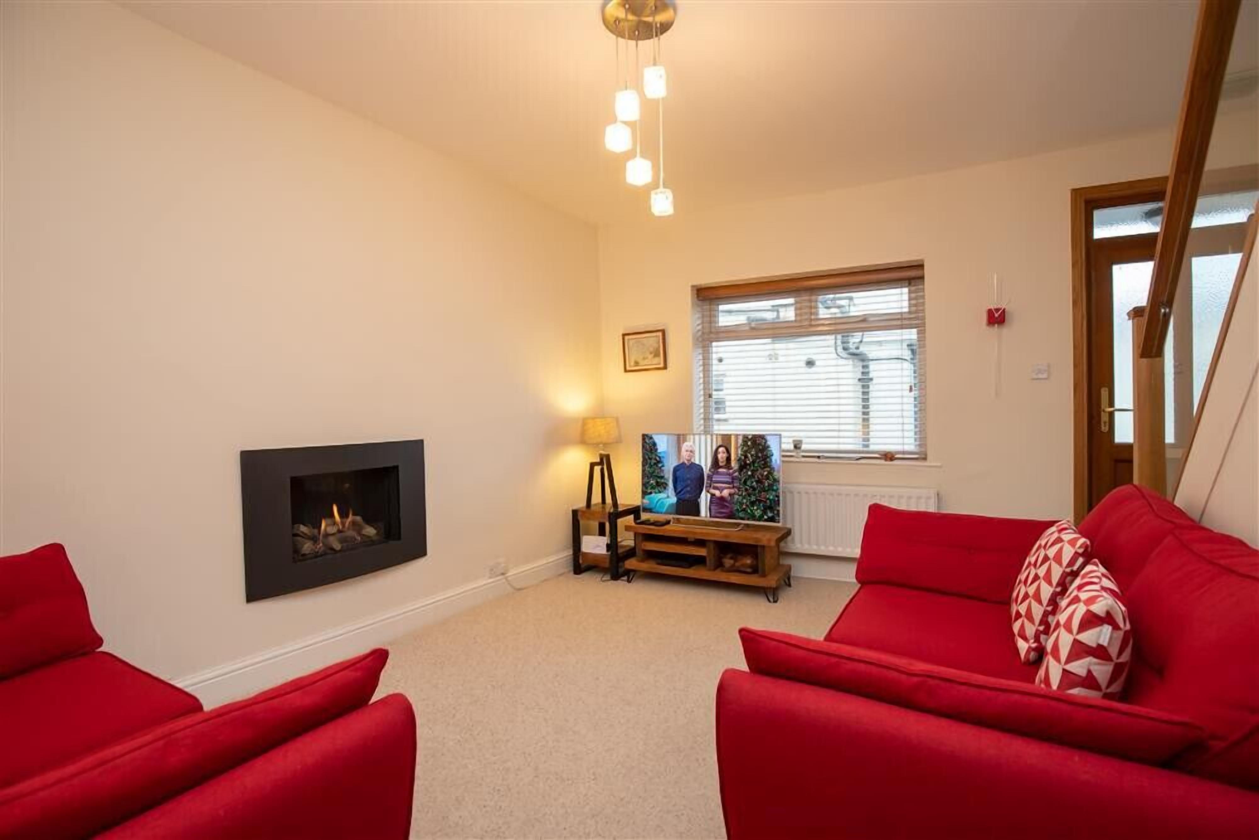 A living room with a fireplace, red sofas, a TV on a wooden stand, and a ceiling light fixture.