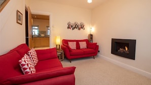 A living room with a red sofa, a fireplace, and a kitchen in the background. - Gable End (Keswick)