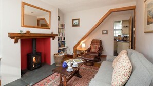 Uma sala de estar aconchegante com lareira, um sofá, uma poltrona de leitura e uma estante de livros.