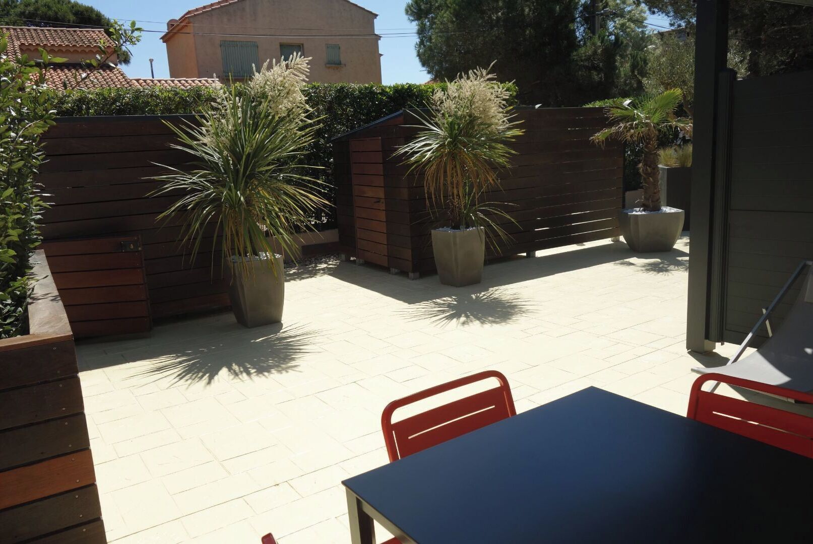 An outdoor patio area with a table and chairs, surrounded by wooden fences and potted plants.