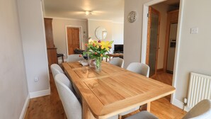 A dining area with a wooden table, grey upholstered chairs, and a vase with flowers. - Silver Birches (Windermere)