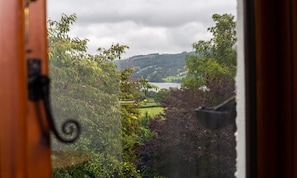 Une vue à travers une fenêtre avec un bouton de porte, dévoilant un paysage composé de collines, d’un lac et d’arbres.