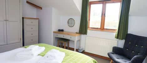 Un dormitorio con cama, escritorio, silla, armario y ventana con cortinas.