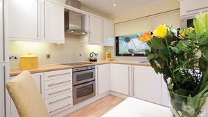 A modern kitchen with white cabinets, a stainless steel range hood, a built-in oven, and a window with a view of the outdoors. - Mount Sol (Ambleside)