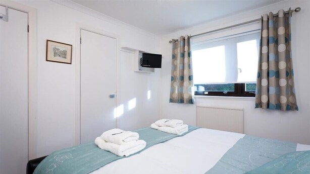 Un dormitorio con cama, televisor, ventana con cortinas e imagen enmarcada en la pared.