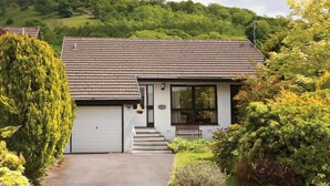 A single-story house with a garage, a front porch, and a view of a green hillside. - Mount Sol (Ambleside)