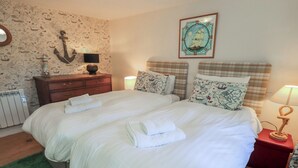 Uma cama de casal com roupa de cama branca, uma cômoda de madeira, uma parede com tema de mapa e uma ilustração de um navio.