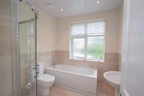 Une salle de bain dotée d’une douche à parois de verre, d’une baignoire, de toilettes et d’une fenêtre donnant sur un espace verdoyant.