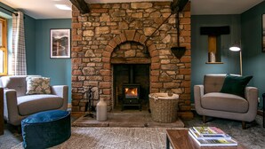 A cozy living room with a stone fireplace, two armchairs, a coffee table, and a bookshelf. - Waltons Close (Penrith)