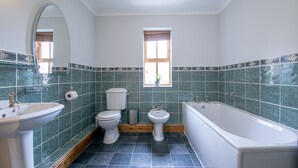 A bathroom with a bathtub, toilet, and sink, featuring green tiles and a window. - Waltons Close (Penrith)