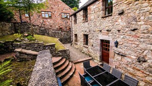 A stone building with a courtyard, stone steps, and outdoor seating. - Waltons Close (Penrith)