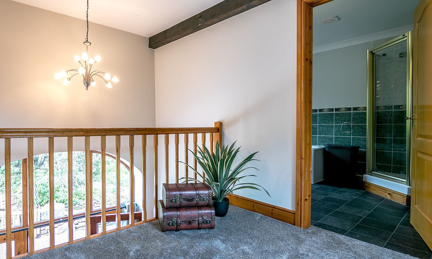 Una escalera con barandilla de madera, un candelabro, una planta en maceta y equipaje apilado.