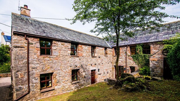A stone building with multiple windows and a tree in front. - Waltons Close (Penrith)