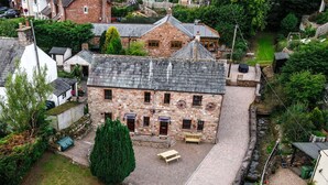 A stone building with a courtyard, surrounded by greenery and other residential structures. - Waltons Close (Penrith)