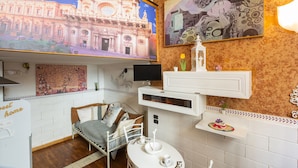 A room with a bed, a small table with a cup and saucer, a TV, and a mural of a building. - 2417 Dimora Santa Croce by Barbarhouse (Lecce)