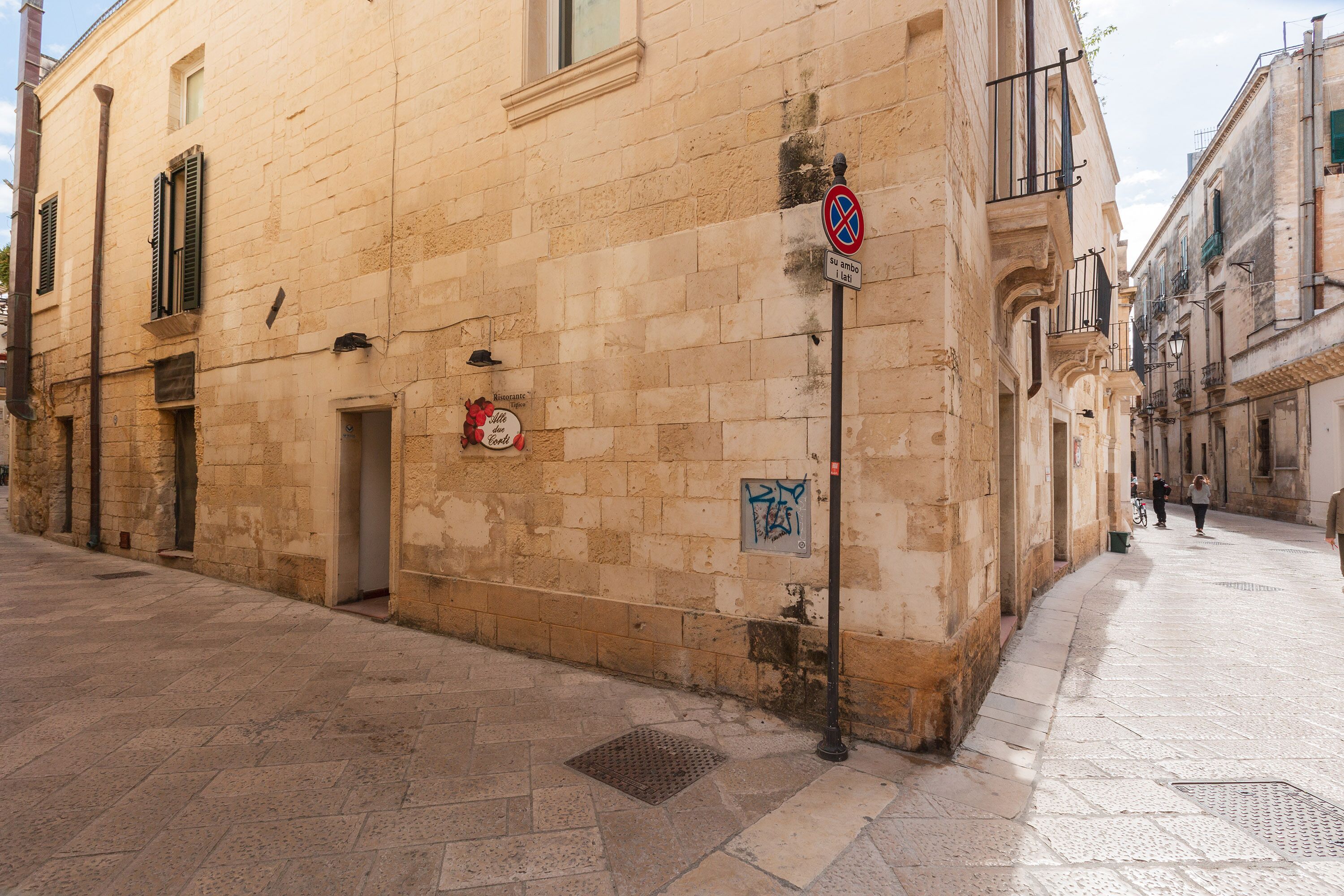 Une rue étroite bordée de bâtiments historiques, un panneau indiquant l’interdiction de se garer et une grille métallique sur le trottoir.