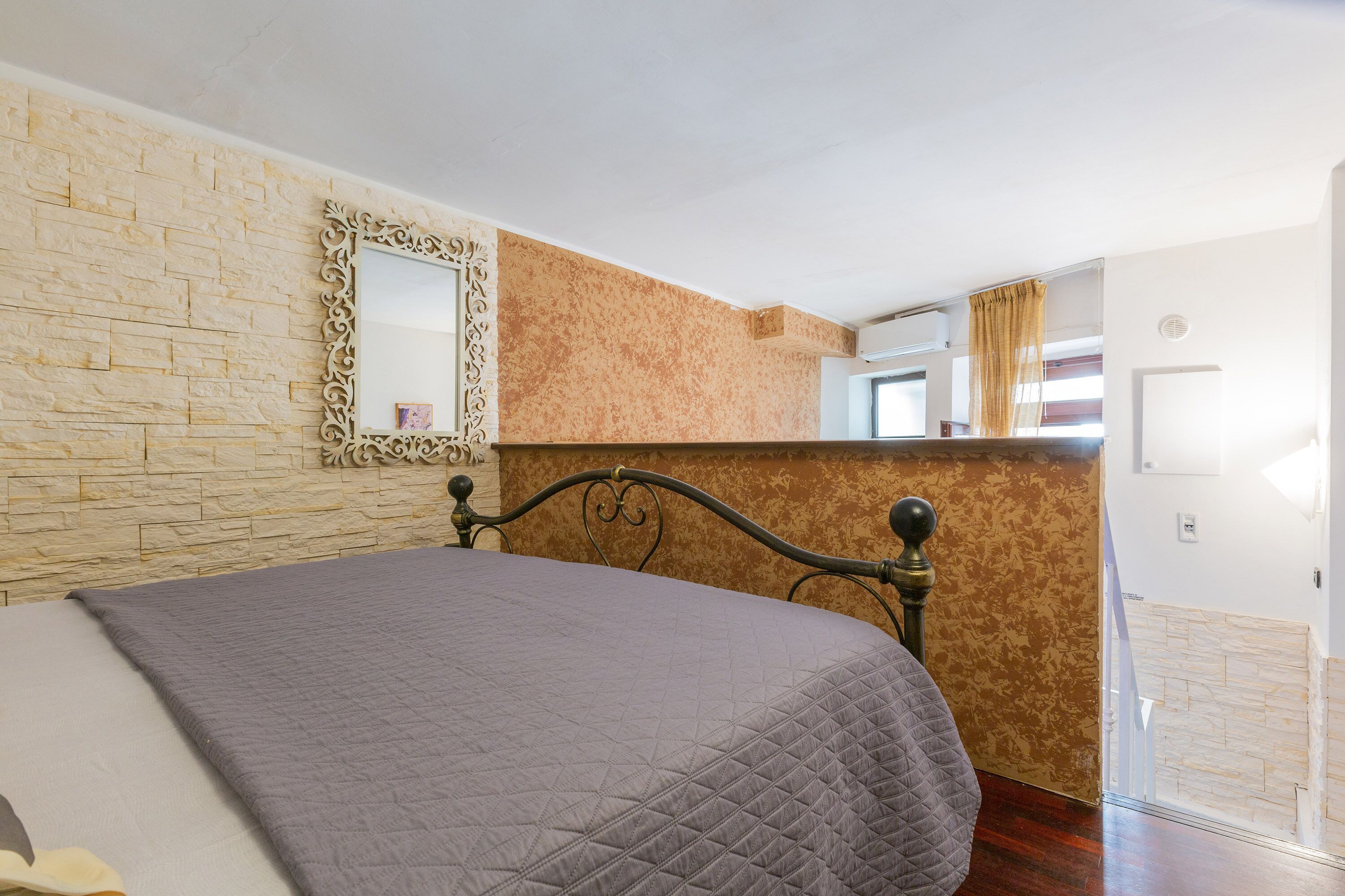 A bedroom with a bed, a mirror, and a textured wall.