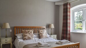 Una cama bien tendida con cabecera de madera, dos mesitas de noche con lámparas y una ventana con cortinas.