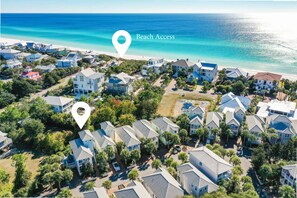 An aerial view of a coastal residential area with houses, a beach, and a marked location for beach access.