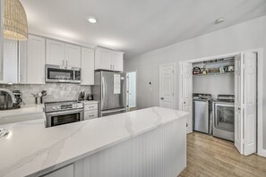 A modern kitchen with white cabinetry, stainless steel appliances, and a marble countertop.