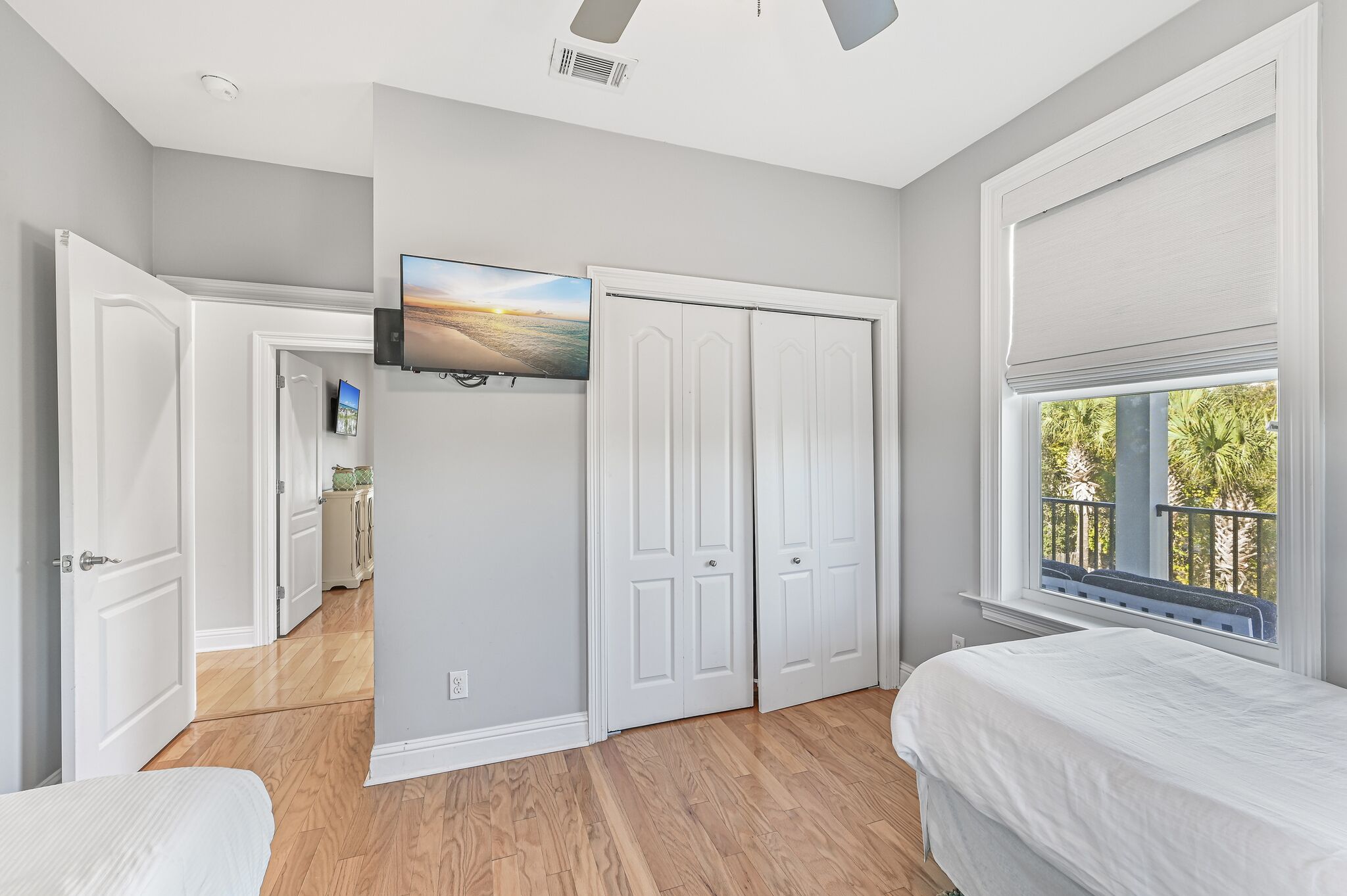 A bedroom with a bed, a TV mounted on the wall, a closet, and a window with a view of trees.