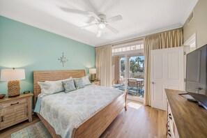 A bedroom with a wooden bed, a ceiling fan, a TV, and a view of the outdoors. - FREE Daily Golf! Reflections 211 Bayfront Beauty, Heated Resort Pool, Hot Tub (Panama City)