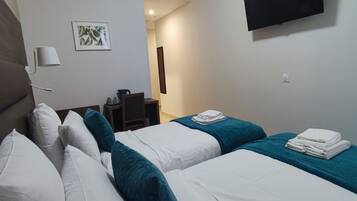 Een hotelkamer met twee bedden, een aan de muur bevestigde televisie, een nachtkastje met een lamp en een lijst aan de muur.