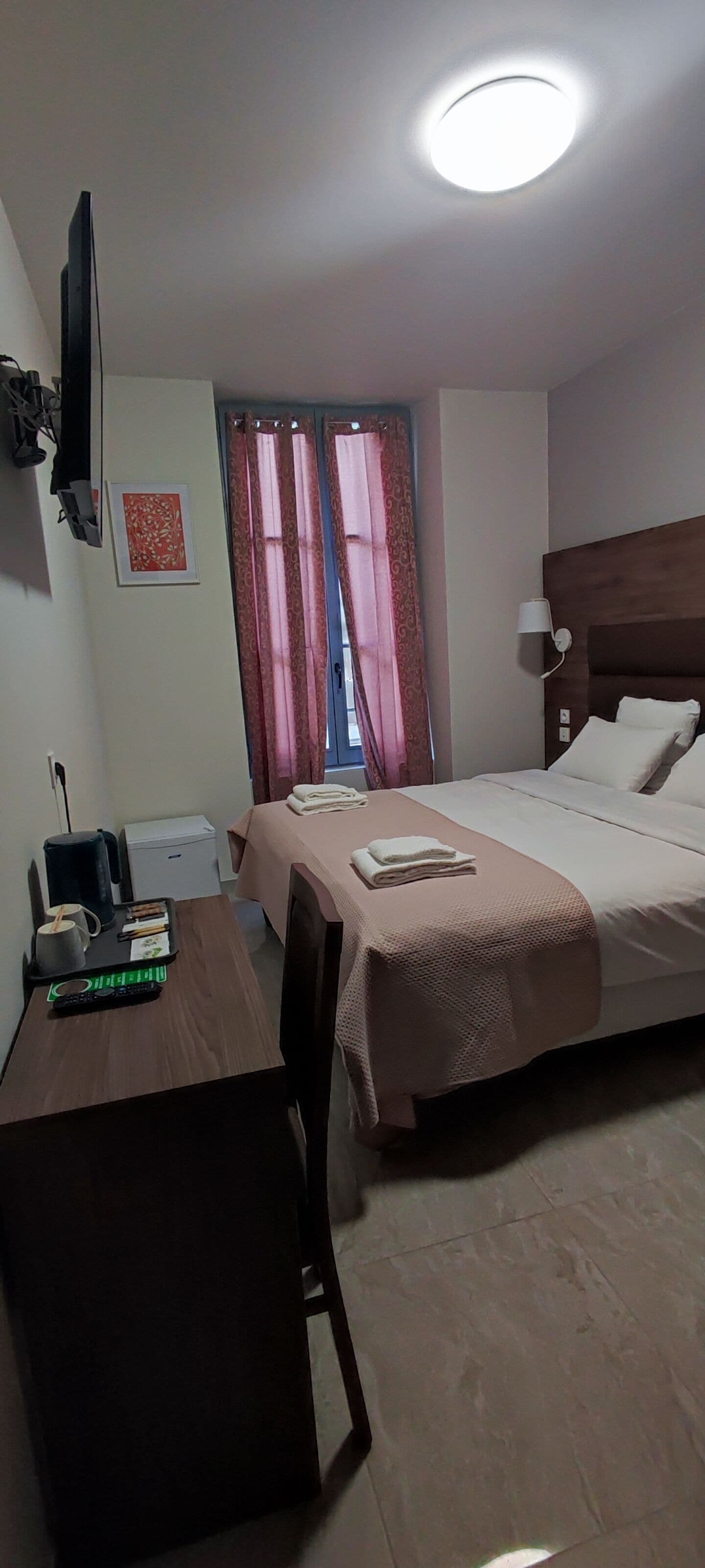 Une chambre d’hôtel comprenant un lit, un bureau avec une chaise, une machine à café, une télévision et une fenêtre avec des rideaux.
