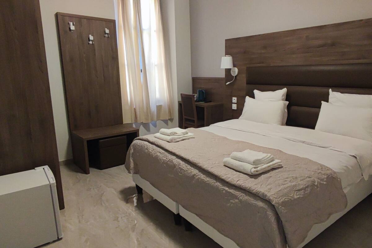 A hotel room with a large bed, a wardrobe, a desk, and a small refrigerator.