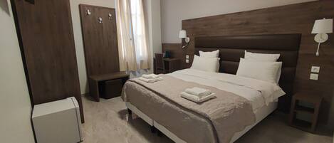 A hotel room with a large bed, a wardrobe, a desk, and a small refrigerator.