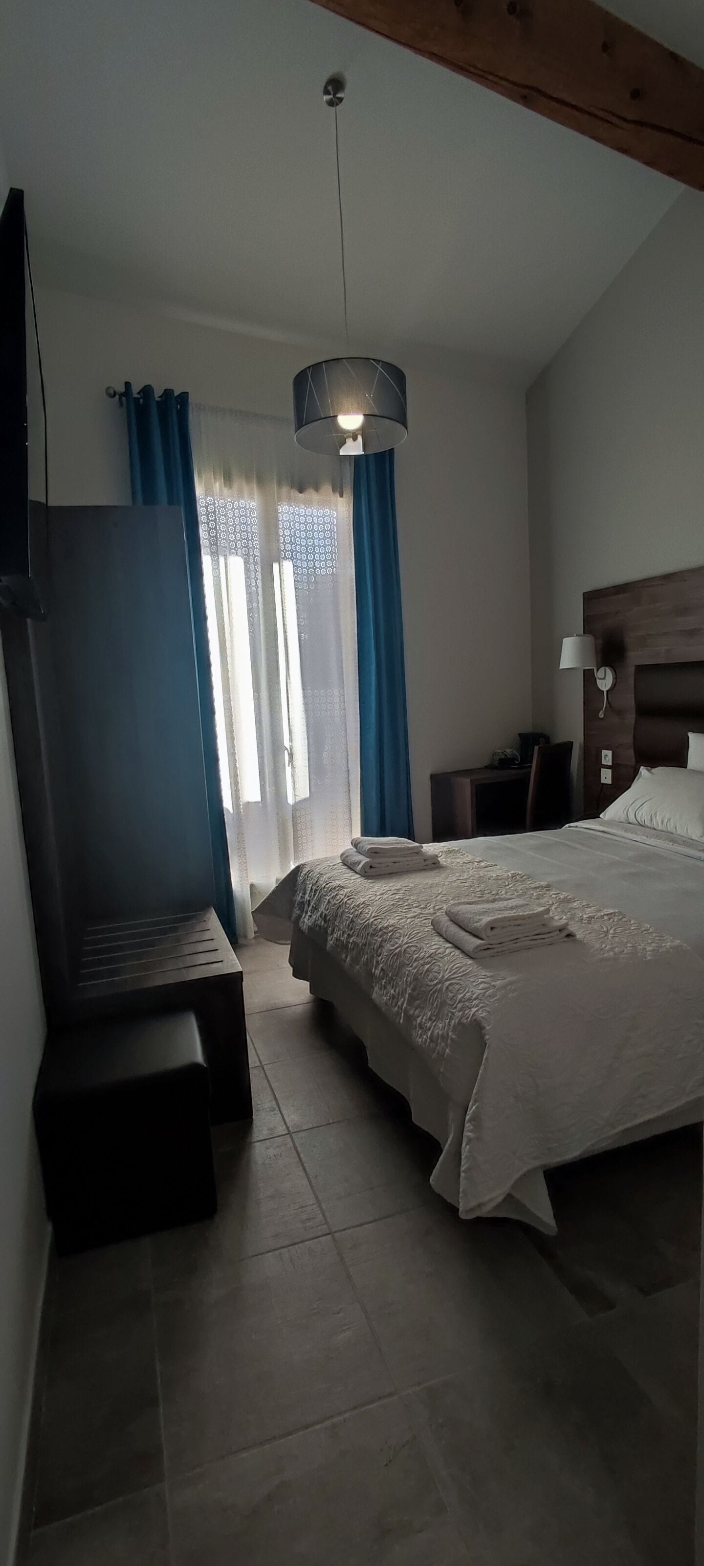 A bedroom with a bed, a desk, a chair, and a hanging light fixture.