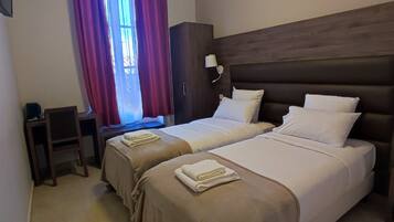 A hotel room with two beds, a desk, a wardrobe, and a window with curtains.